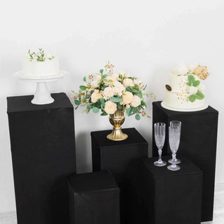 Decorative cakes and floral arrangement on black pedestals in a styled setting.
