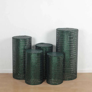 Green decorative cylindrical vases in various heights on a plain backdrop.