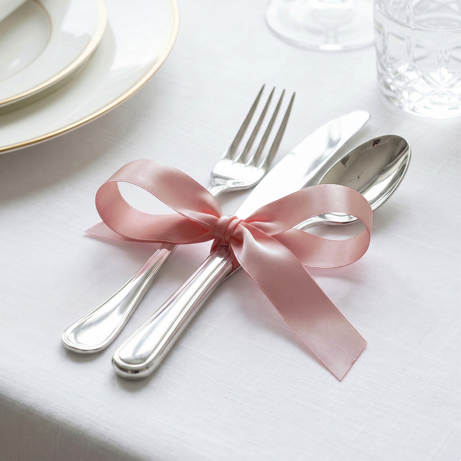 Pink ribbon tied around silver cutlery on elegant white table setting
