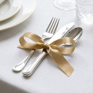Gold ribbon tied around silver cutlery on elegant white table setting