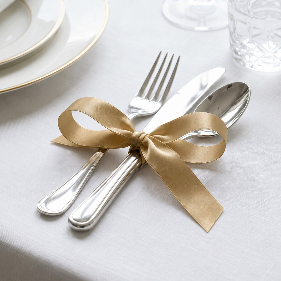 Gold ribbon tied around silver cutlery on elegant white table setting