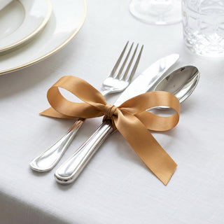 Elegant gold ribbon tied around silver cutlery on a white table setting