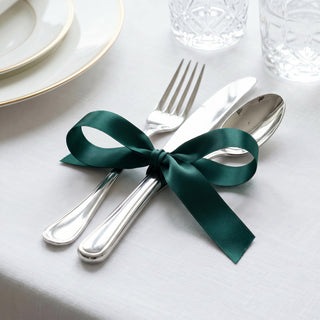 Elegant table setting with silver cutlery tied by a green ribbon on white tablecloth