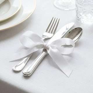Elegant white ribbon tied around silver fork and spoon on a formal table setting