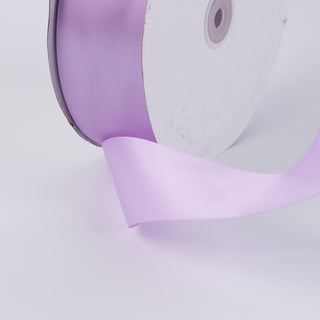 Lavender satin ribbon spool with ribbon unrolling on white background
