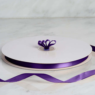 Purple satin ribbon spool with decorative bow on a white surface