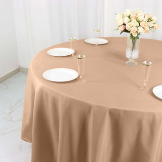 Elegant beige tablecloth draped over a round table with plates and glasses.