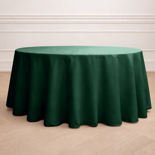 Green round tablecloth with elegant draping on a wooden floor.
