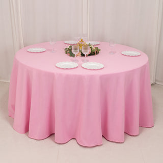 Round pink tablecloth draped over a table with decorative plates and glasses.