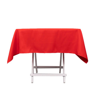 Red tablecloth draped over a folding table on a plain backdrop