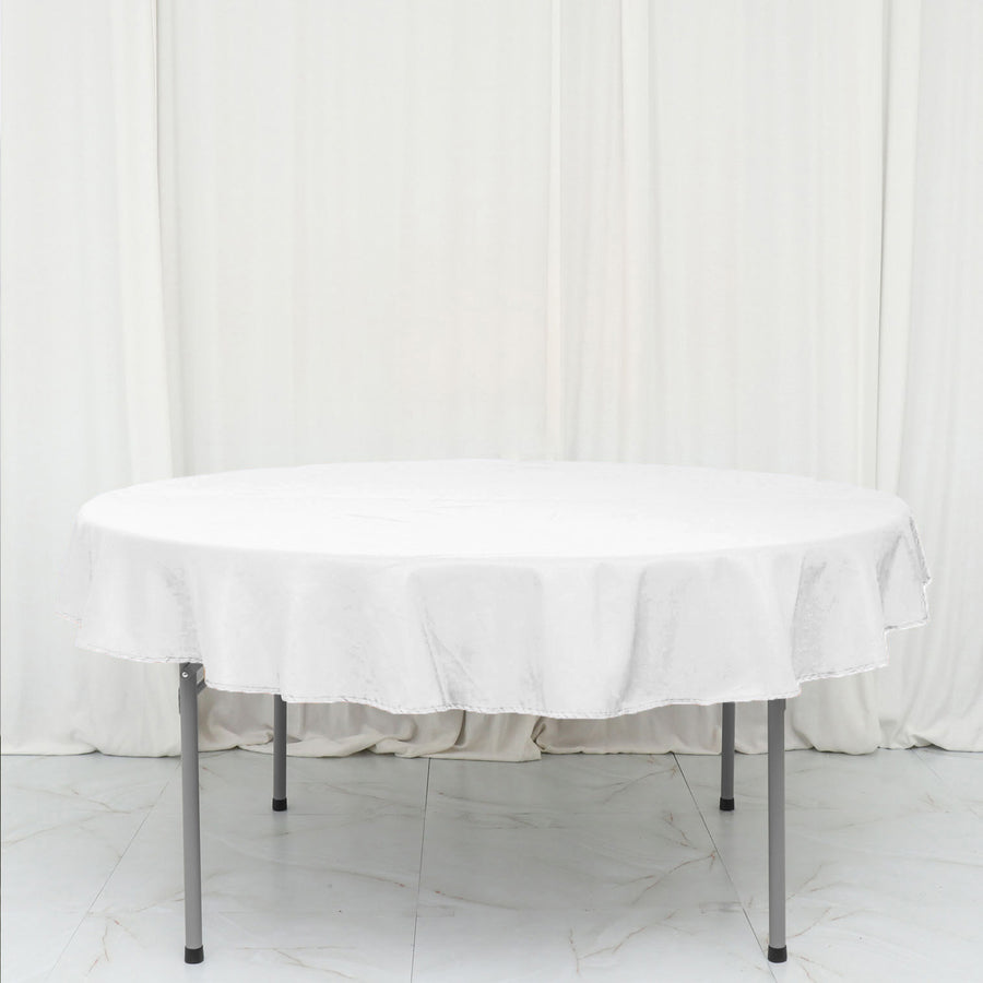 Round white table with a tablecloth, set against a plain backdrop.