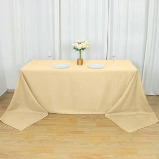 Beige tablecloth draped over a table with plates and glasses.