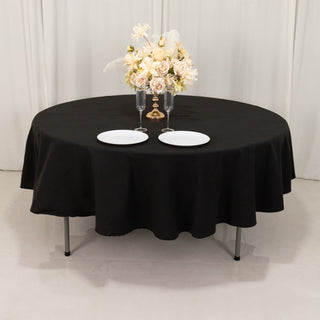 Round black tablecloth on a table set with plates and a floral centerpiece.