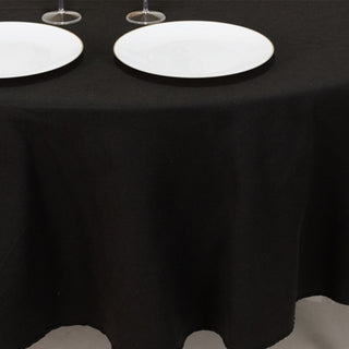 Black tablecloth draping over a round table with white plates on top.