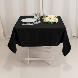 Black tablecloth draped over a table with glassware, plates, and flowers.