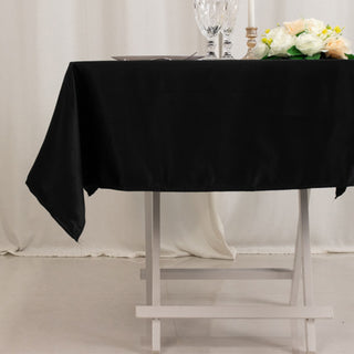 Black tablecloth draped over a white table, set for dining with flowers and glassware.
