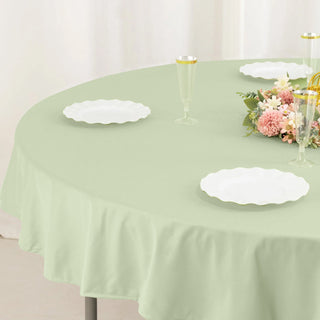 Green tablecloth on a round table set with white plates and floral centerpiece.