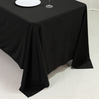 Black tablecloth draping over a table with a plate and glass on a light surface.