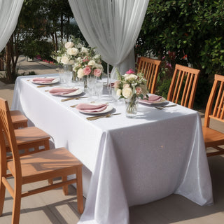 Elegant outdoor dining setup with floral centerpieces and sparkling tablecloth.