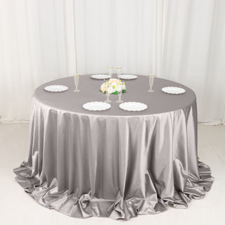 Elegant round table with a gray satin tablecloth and white plates for special occasions.