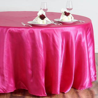 Pink satin tablecloth draped over round table with elegant napkin presentation.