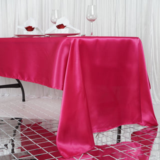 Pink satin tablecloth draped elegantly on a dining table with glasses and napkins.