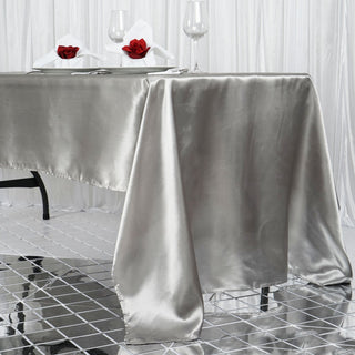 Elegant silver satin tablecloth draping over a dining table with decor.