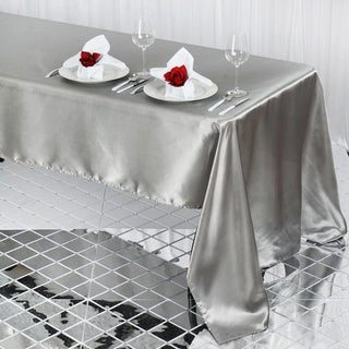 Elegant silver satin tablecloth draping over a glass table setting with roses.