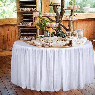 Elegant dessert table with white tablecloth and rustic decor in a wooden setting.