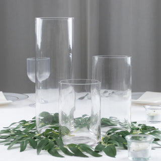 Clear glass vases arranged with greenery on a table setting.