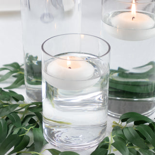 Floating candle in a glass surrounded by greenery and additional glass vases.