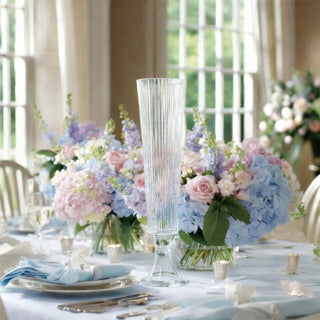 Elegant tall crystal vase surrounded by pastel floral arrangements on a dining table.