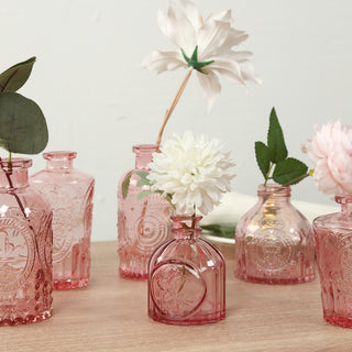 Assorted pink glass vases with flowers on a wooden table.