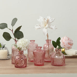Assorted vintage pink glass vases with floral arrangements and greenery.