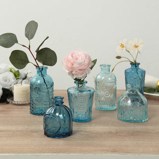 Assorted blue decorative glass vases with flowers on a wooden table.