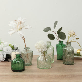 Assorted green glass vases with flowers on a wooden table.