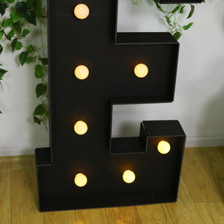 Black marquee letter 'E' with glowing bulbs, styled with greenery.