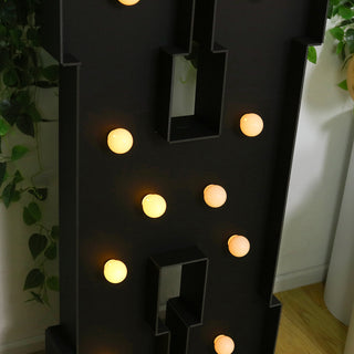 Decorative marquee letter with warm glowing lights on a dark background.