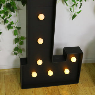 Black letter "L" marquee light with warm bulbs on a wooden floor.