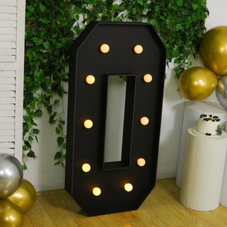 Large marquee letter "O" with lights, set against greenery and balloons.