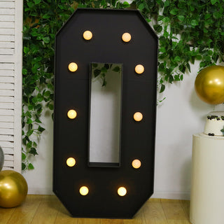 Decorative marquee number "0" with lights on a green and gold party backdrop.