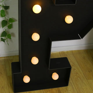 Black letter "P" with glowing bulbs on a wooden floor.