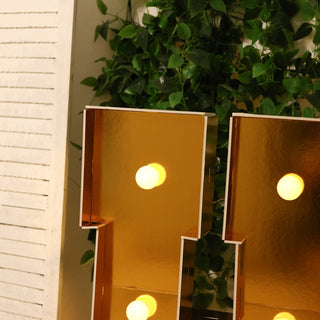 Gold marquee letters with bulbs, surrounded by greenery.