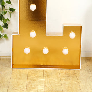 Gold marquee letter with white bulbs on a wooden floor.