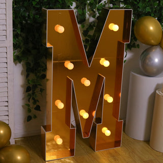 Gold letter "M" marquee sign with lights in a festive setting.