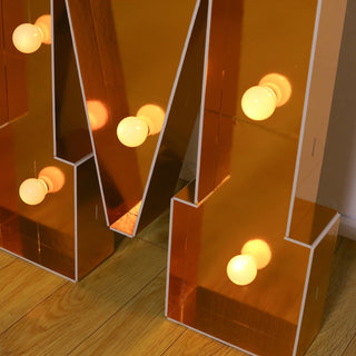 Gold marquee letter "M" with vintage bulbs on wooden floor.