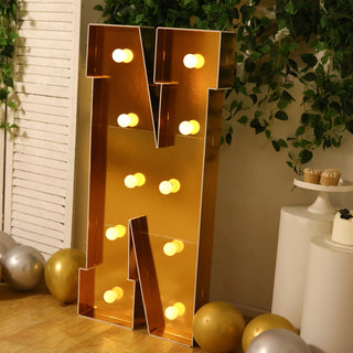 Gold marquee letter "N" with lights, surrounded by balloons and greenery.