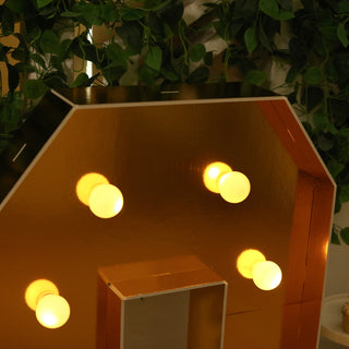 Gold marquee letter with glowing bulbs against a green backdrop.