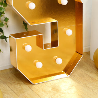 Gold marquee letter "S" with light bulbs on a wooden floor.