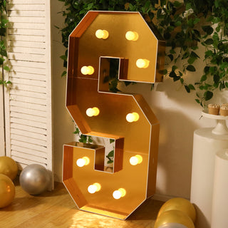 Gold marquee letter "S" with lights, decorated with greenery and balloons.